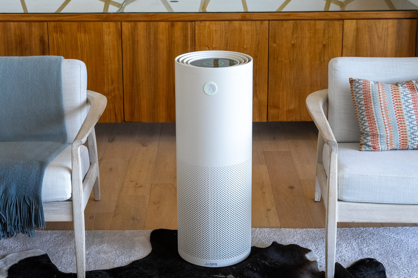 Jaspr air purifier in living room between two arm chairs with sideboard in the background