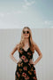 Woman wearing a floral dress and sunglasses against a light blue sky.