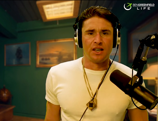 Ben Greenfield wearing headphones and speaking into a microphone in a room with green walls and framed pictures.