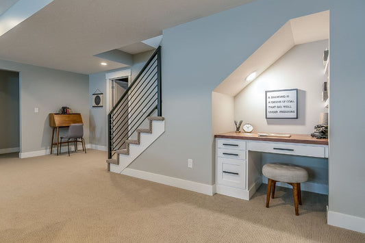 Photo of a finished basement with blue walls. We see a desk nook under the stairs and the stairs.