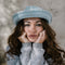 Woman wearing a blue knit hat and sweater with a blurred background